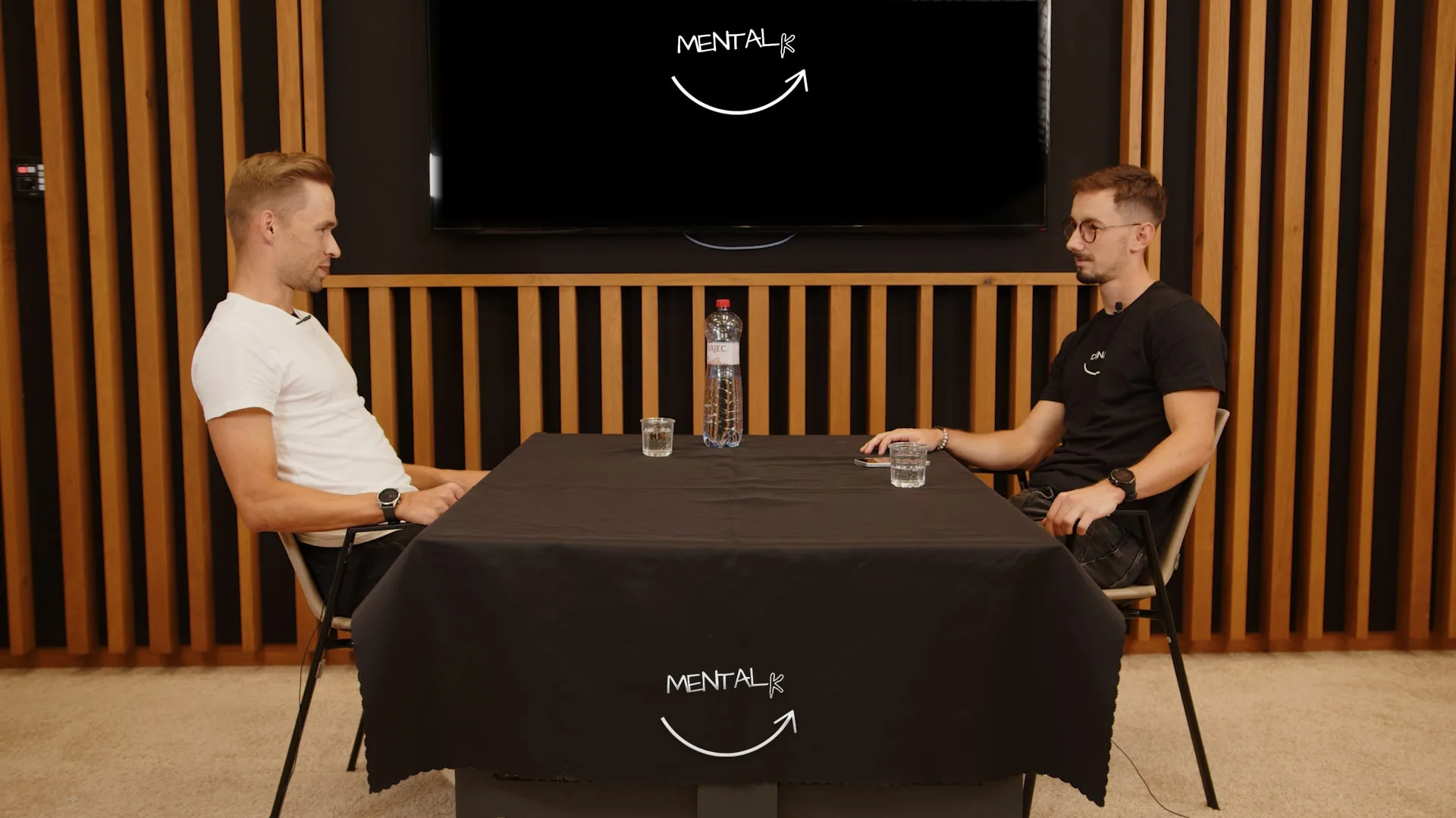 Dvaja hostia podcastu MENTALK v modernom štúdiu počas rozhovoru pri stole s logom